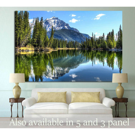 Reflective Pine Forest and Mountain Range Canvas for Rustic DecorThis canvas print portrays the tranquil beauty of a mountain lake, reflecting the crisp image of the surrounding pines and the imposing mountain range. The clear blue sky and the still water