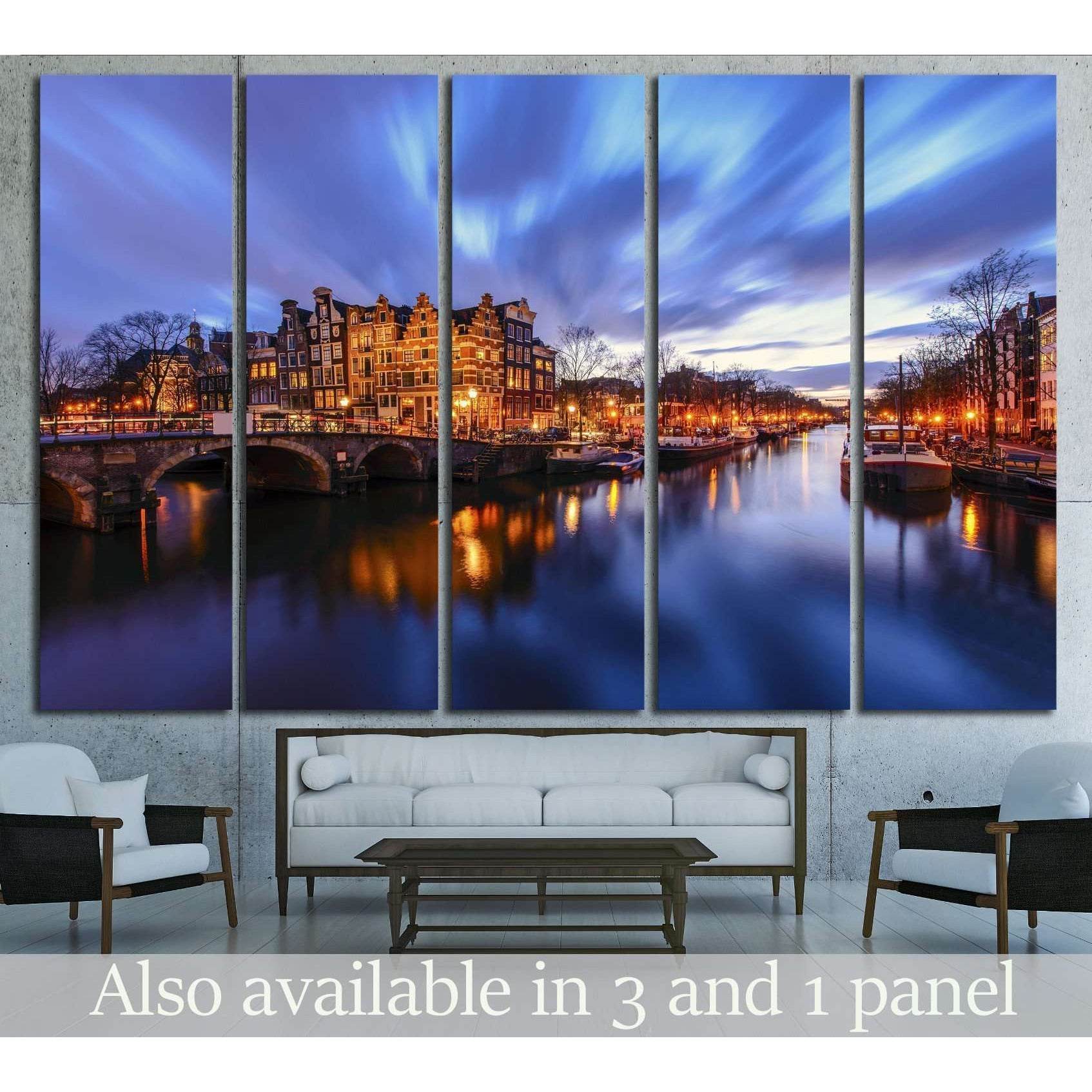 Amsterdam canal canvas print at twilight with glowing bridge lights above a sofa in a modern living room
