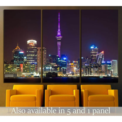 Auckland skyline triptych canvas print with Sky Tower lit purple at night, displayed above yellow chairs