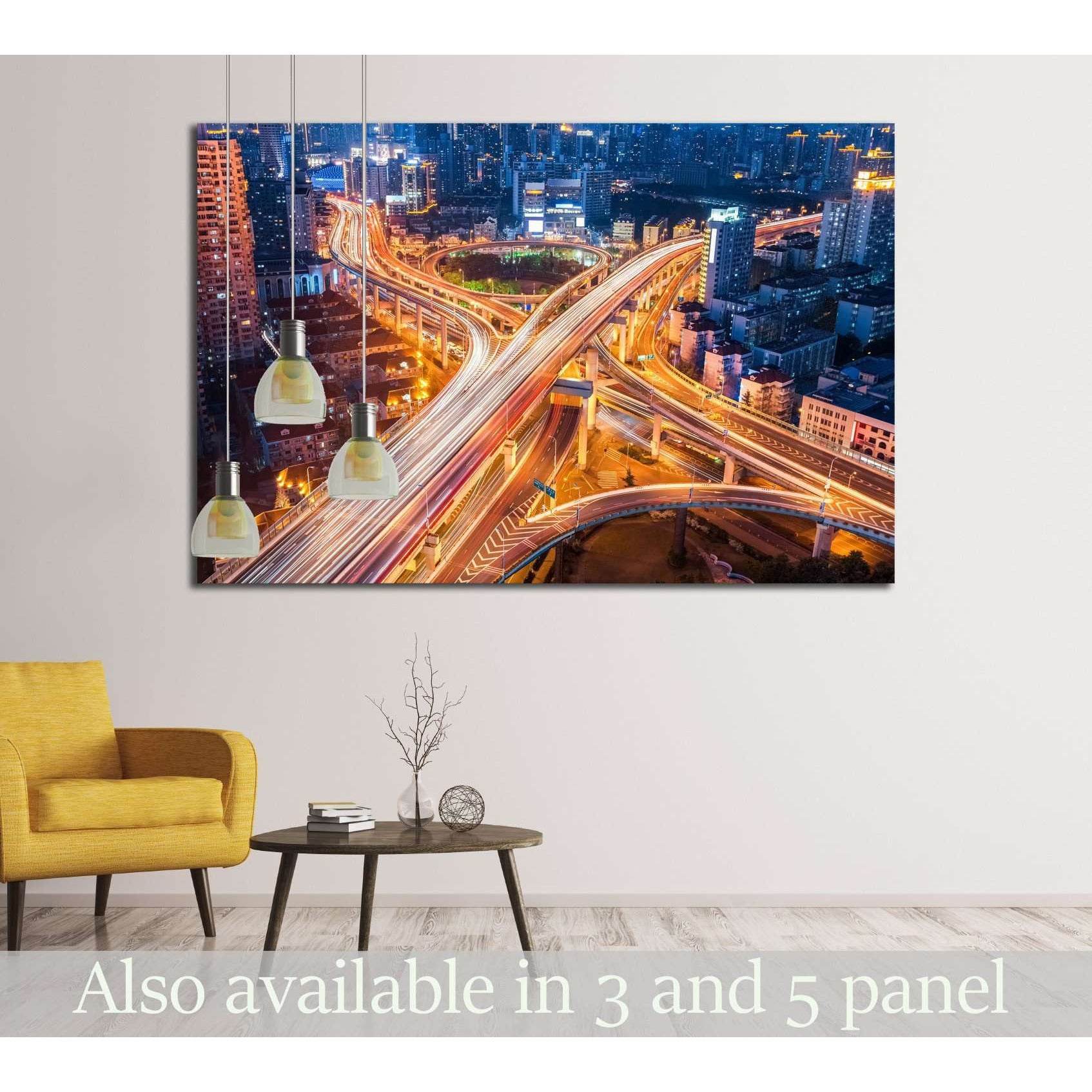Night city interchange canvas print with glowing highway light trails above chair in a modern living room