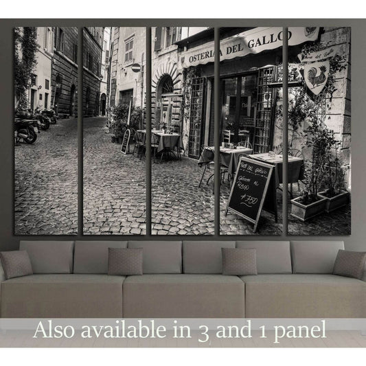 Black and white Rome street canvas print with cobbled lane and osteria, displayed above a sofa in a modern living room