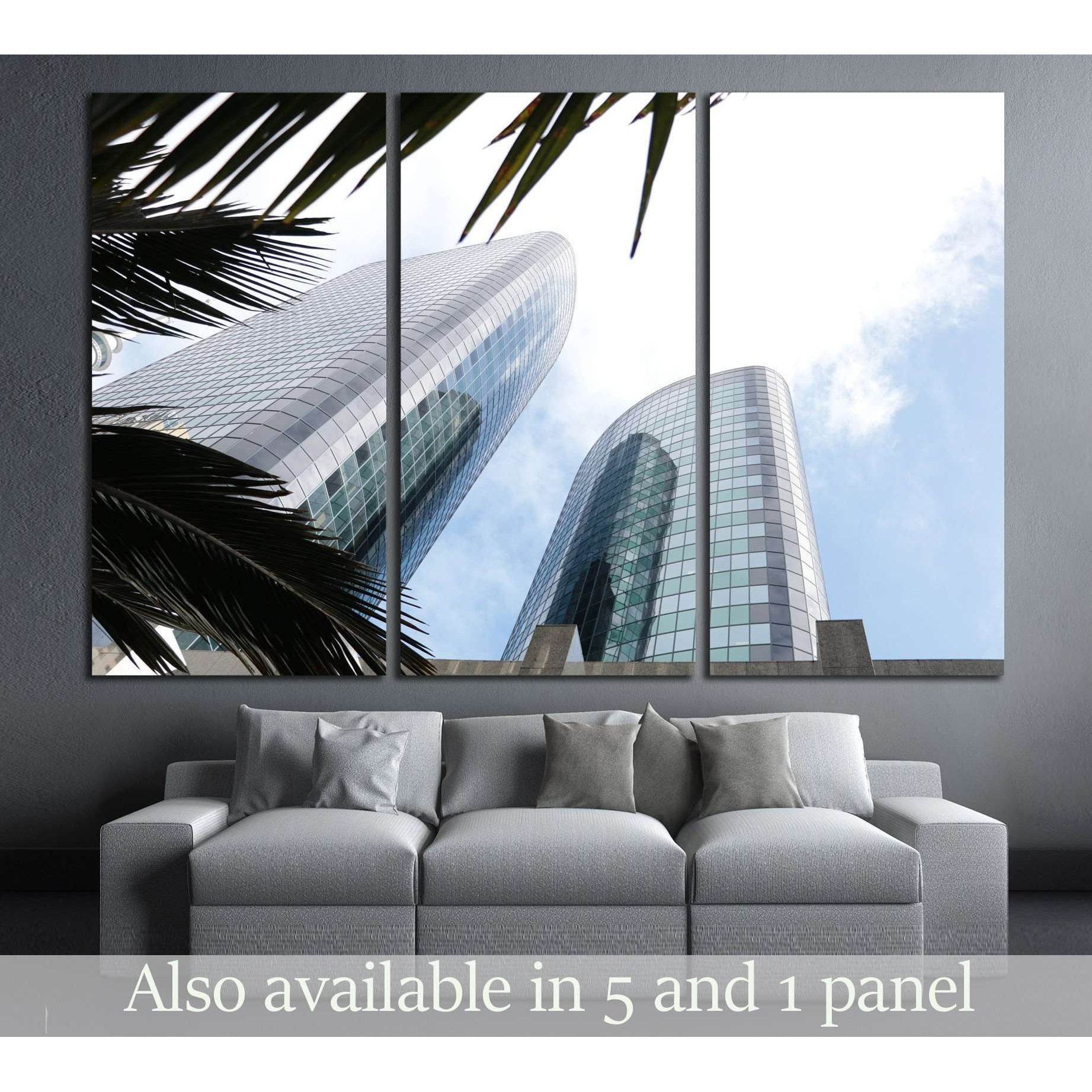 Blue glass skyscraper canvas print with palm fronds, shown above sofa in a modern living room
